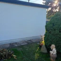 Biała elewacja domu jednorodzinnego w słoneczny dzień, widok z ogrodu z rzeźbą aniołka. Świeżo pomalowana ściana budynku.