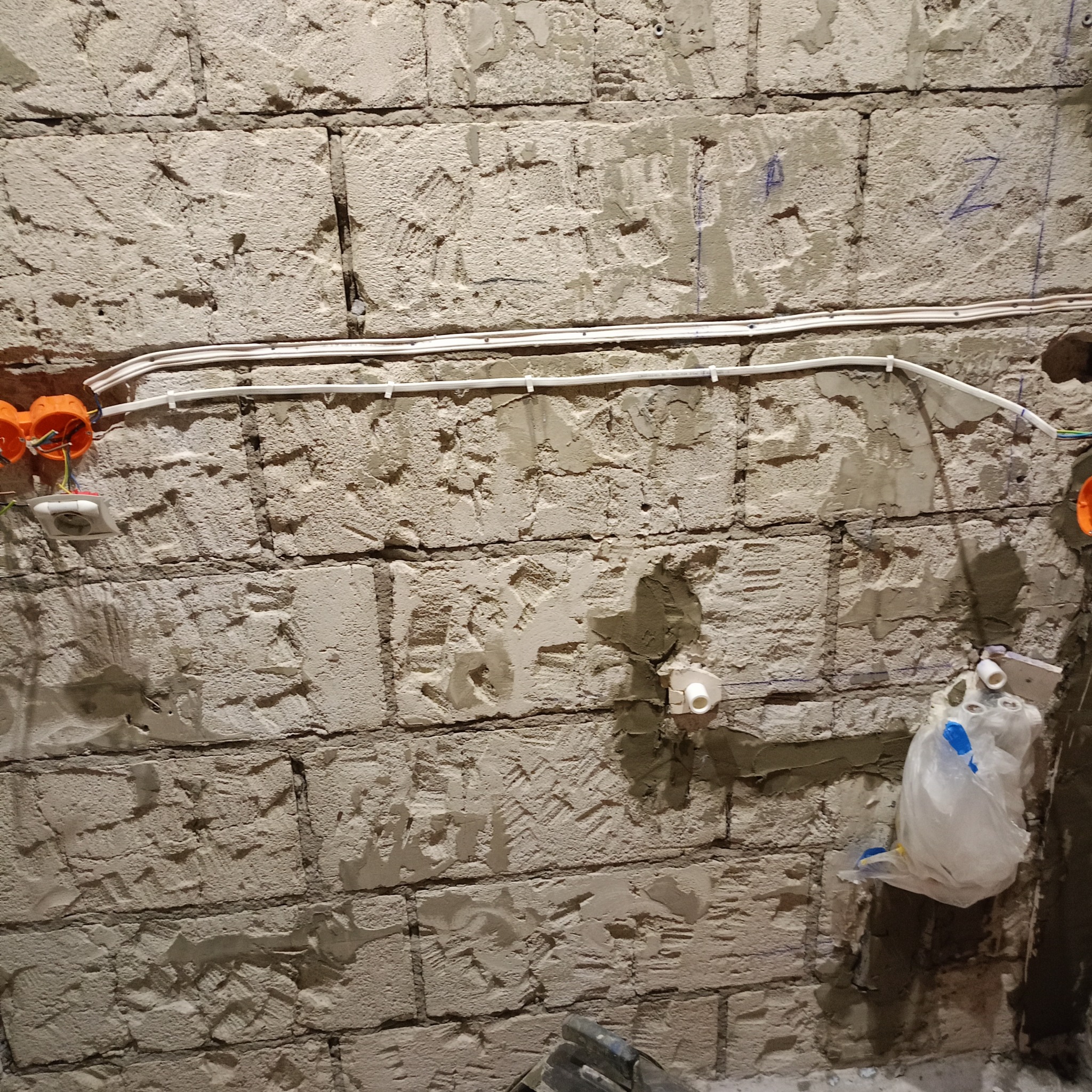 Surowa ściana z cegły w trakcie remontu łazienki, widoczne nowe instalacje elektryczne w peszlach, puszki elektryczne i przyłącza wodne, przygotowana do dalszych prac wykończeniowych.