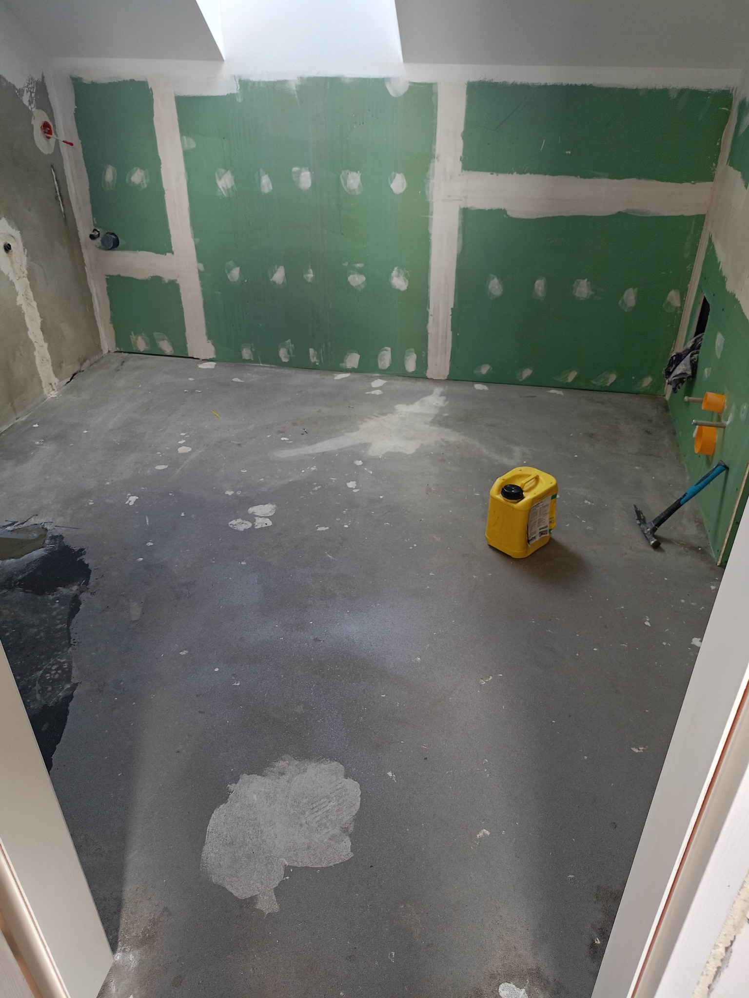 Wnętrze łazienki w trakcie prac: ściany z płyt kartonowo-gipsowych, częściowo zaszpachlowane łączenia, widoczne instalacje hydrauliczne, na podłodze żółty kanister i młotek.