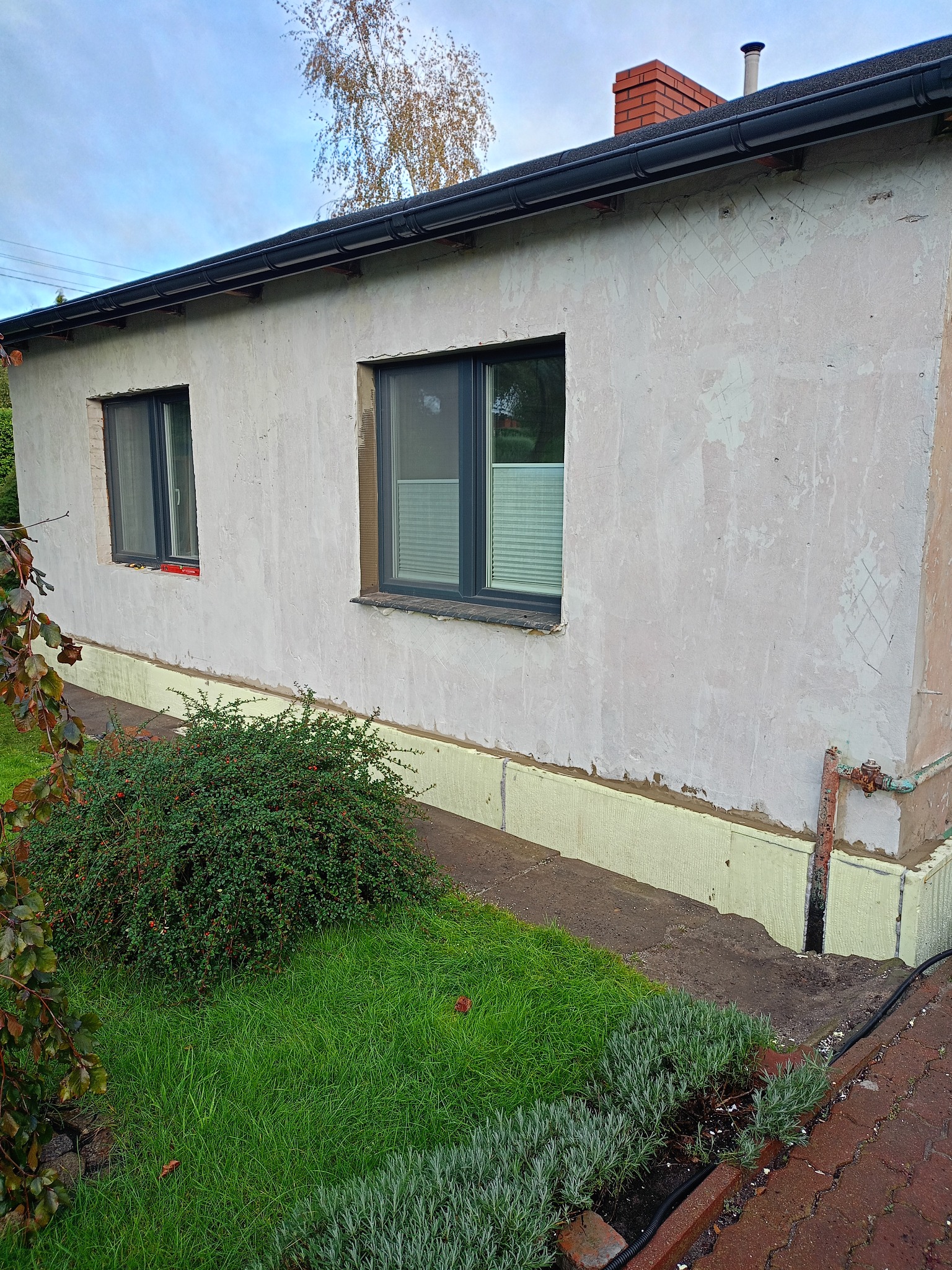 Ocieplenie fundamentów i przygotowanie pod elewację budynku w Lubiczu. Widoczne fragmenty ocieplenia i surowa ściana z dwoma oknami.