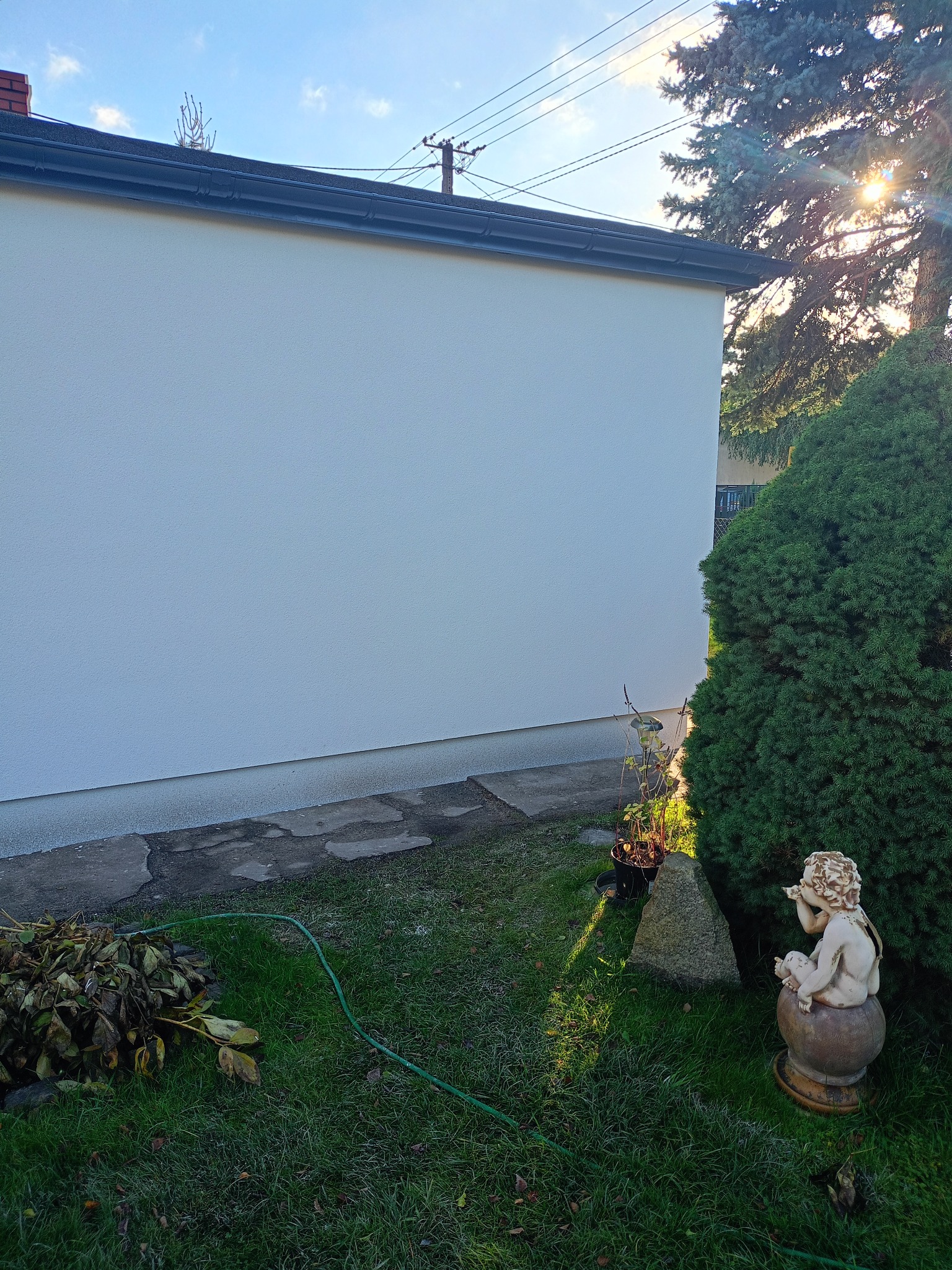 Biała elewacja domu jednorodzinnego w słoneczny dzień, widok z ogrodu z rzeźbą aniołka. Świeżo pomalowana ściana budynku.