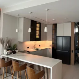 Nowoczesna kuchnia z wyspą: marmurowy blat, drewniane hokery, czarne akcenty i podświetlenie LED. Minimalistyczny design z roślinami i sprzętem AGD.