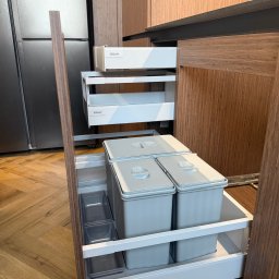 ERNEST STANIK - Otwarta szuflada kuchenna z systemem segregacji odpadów i dwoma wewnętrznymi szufladami Blum, w nowoczesnej zabudowie z ciemnego drewna, na tle podłogi w jodełkę.