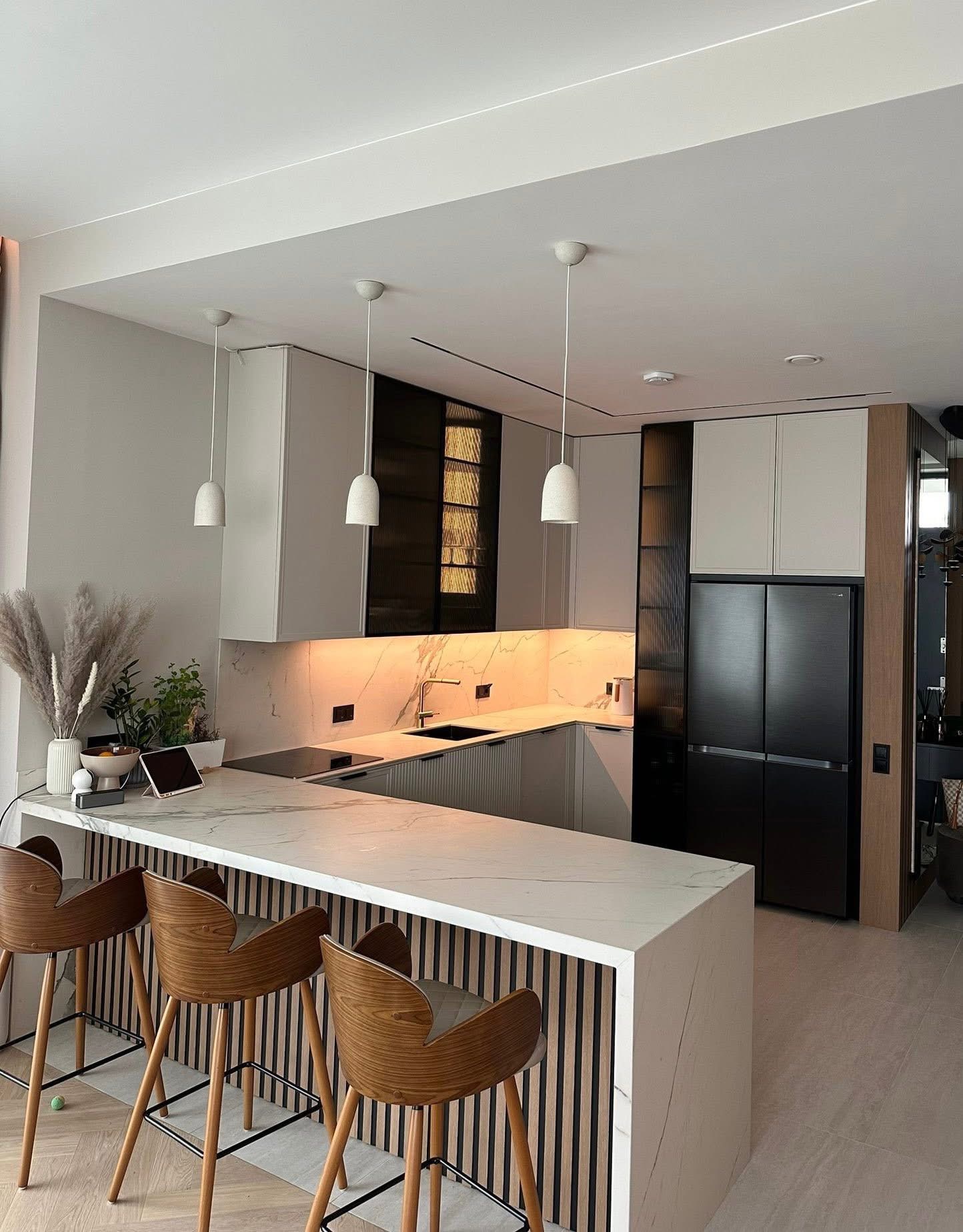 Nowoczesna kuchnia z wyspą: marmurowy blat, drewniane hokery, czarne akcenty i podświetlenie LED. Minimalistyczny design z roślinami i sprzętem AGD.