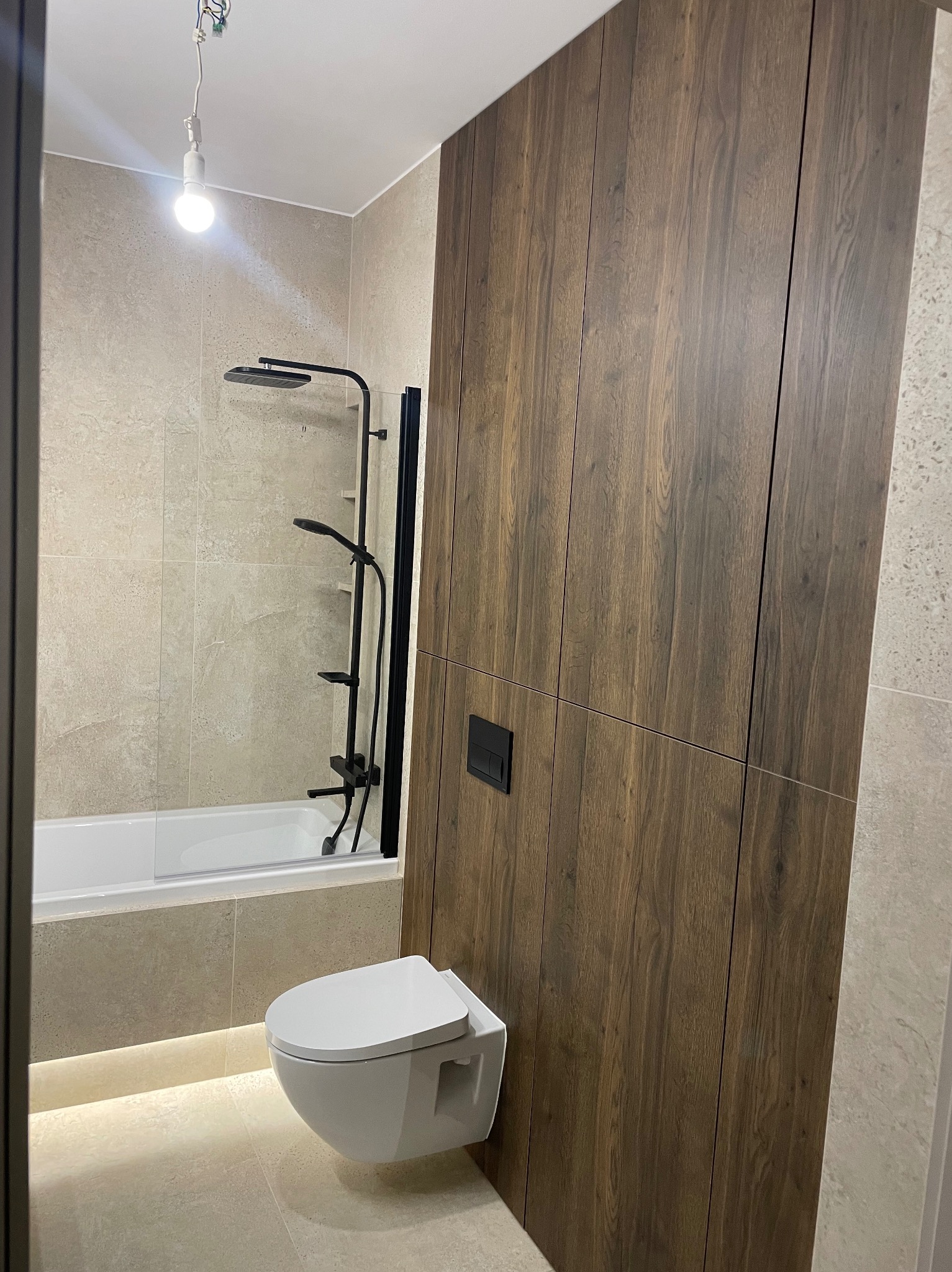 Nowoczesna łazienka z drewnianą zabudową, podwieszaną toaletą i czarną armaturą prysznicową. Minimalistyczny design z subtelnym oświetleniem podłogowym.