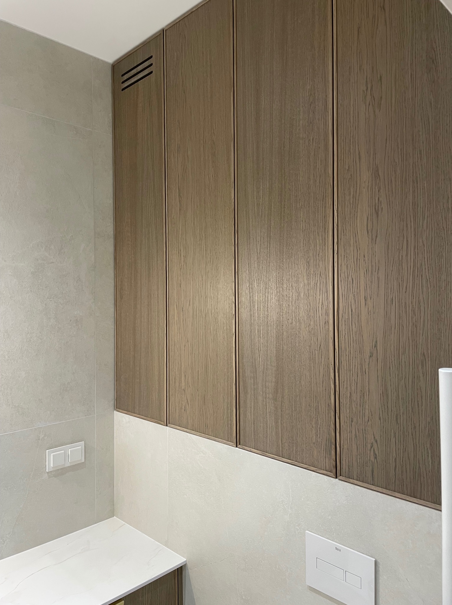 Drewniana szafa wnękowa z czterema drzwiami, zamontowana w łazience z jasnymi płytkami. Widoczne detale wykończenia i wentylacja.