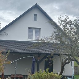 Andrzej Geburek - Dom jednorodzinny z ciemnoszarym dachem z dachówki bitumicznej, widoczny z poziomu ogrodu w pochmurny dzień. Na dachu widoczny komin.