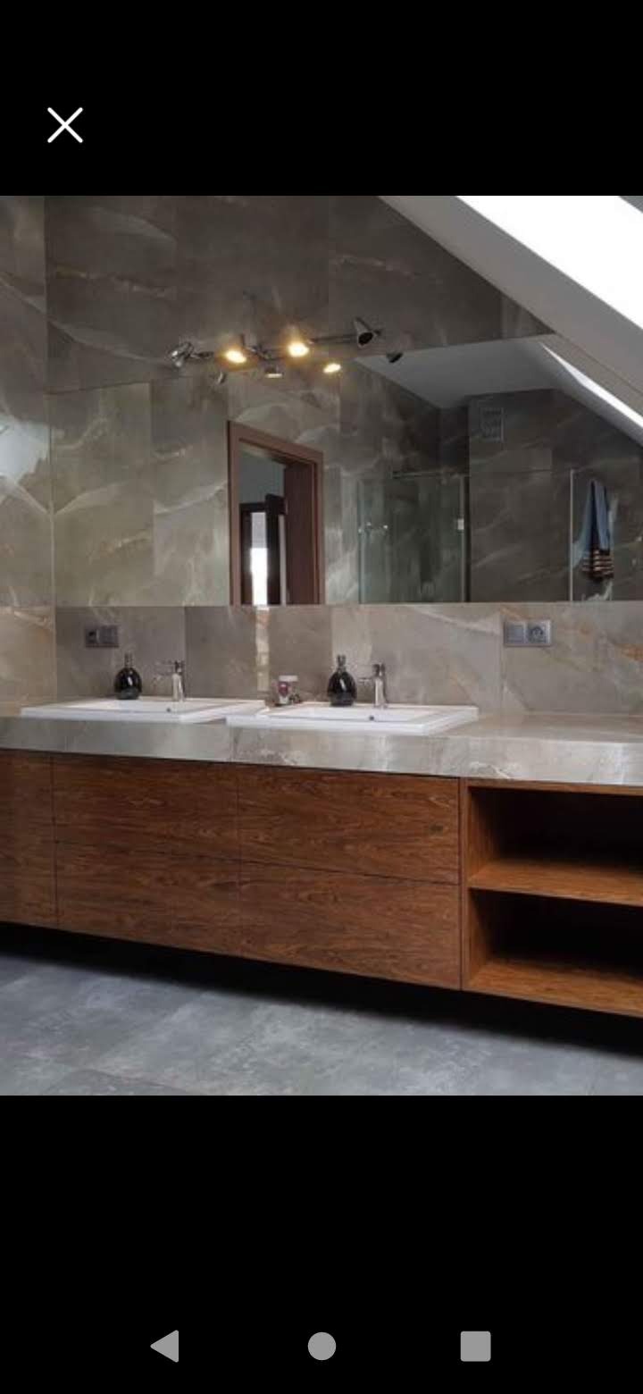 Nowoczesna łazienka z dwoma umywalkami nablatowymi, drewnianą szafką pod umywalką z otwartymi półkami, dużym lustrem i marmurowymi płytkami na ścianach, oświetlona halogenami.