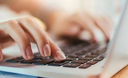 Dłonie kobiety piszącej na laptopie, skupienie na klawiaturze i palcach z jasnym manicure.