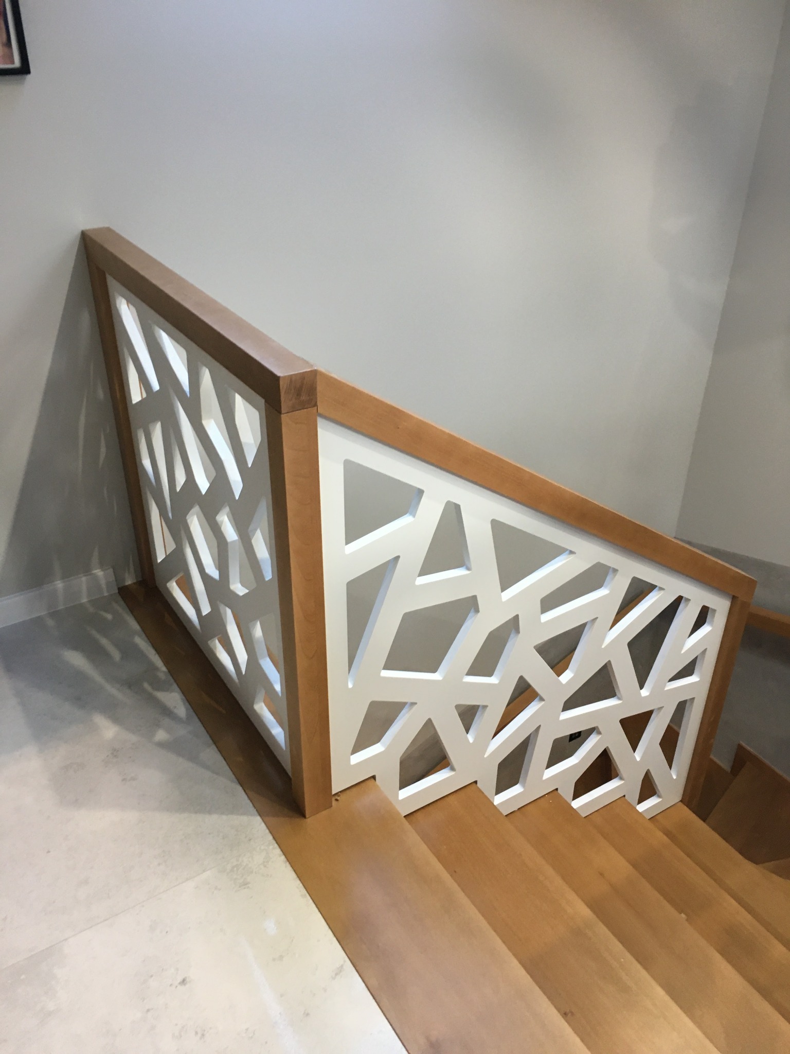 Nowoczesna balustrada schodowa z jasnego drewna i białym, geometrycznym wypełnieniem, widok z góry na drewniane stopnie.