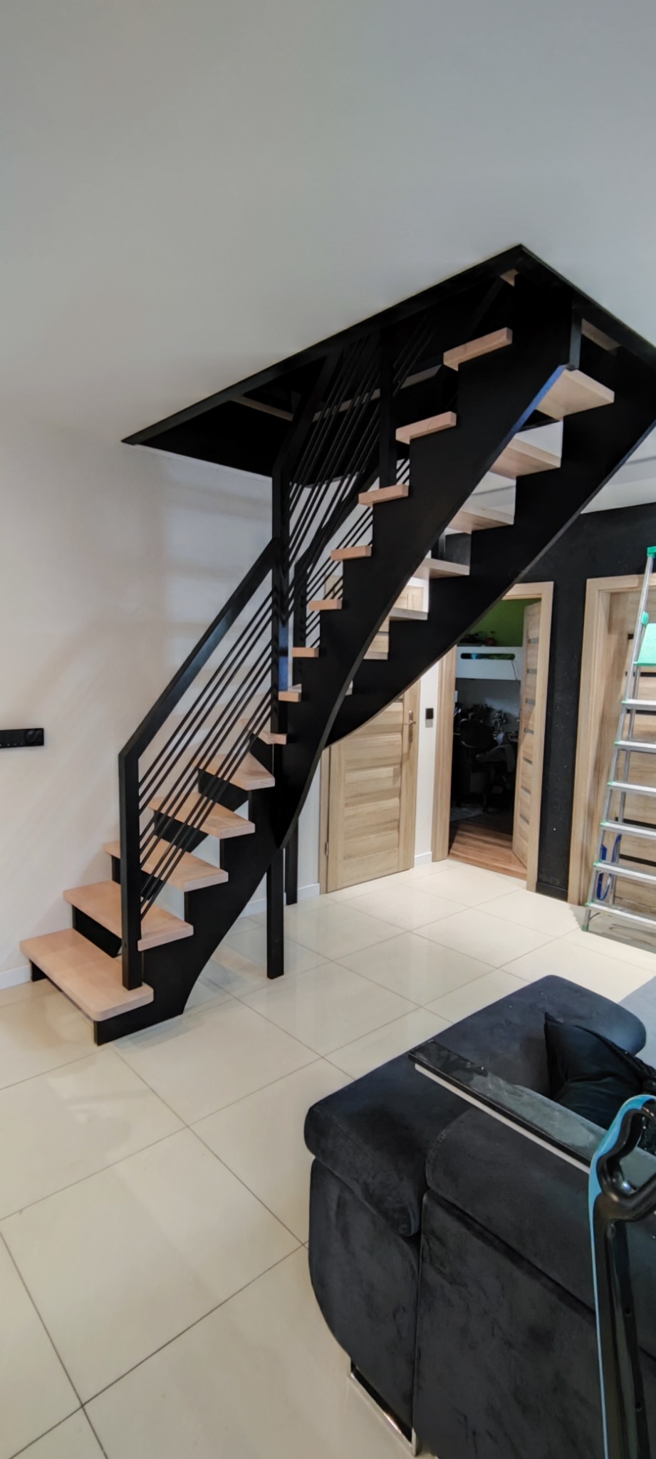 Nowoczesne schody z czarną metalową konstrukcją i jasnymi drewnianymi stopniami w jasnym wnętrzu domu.