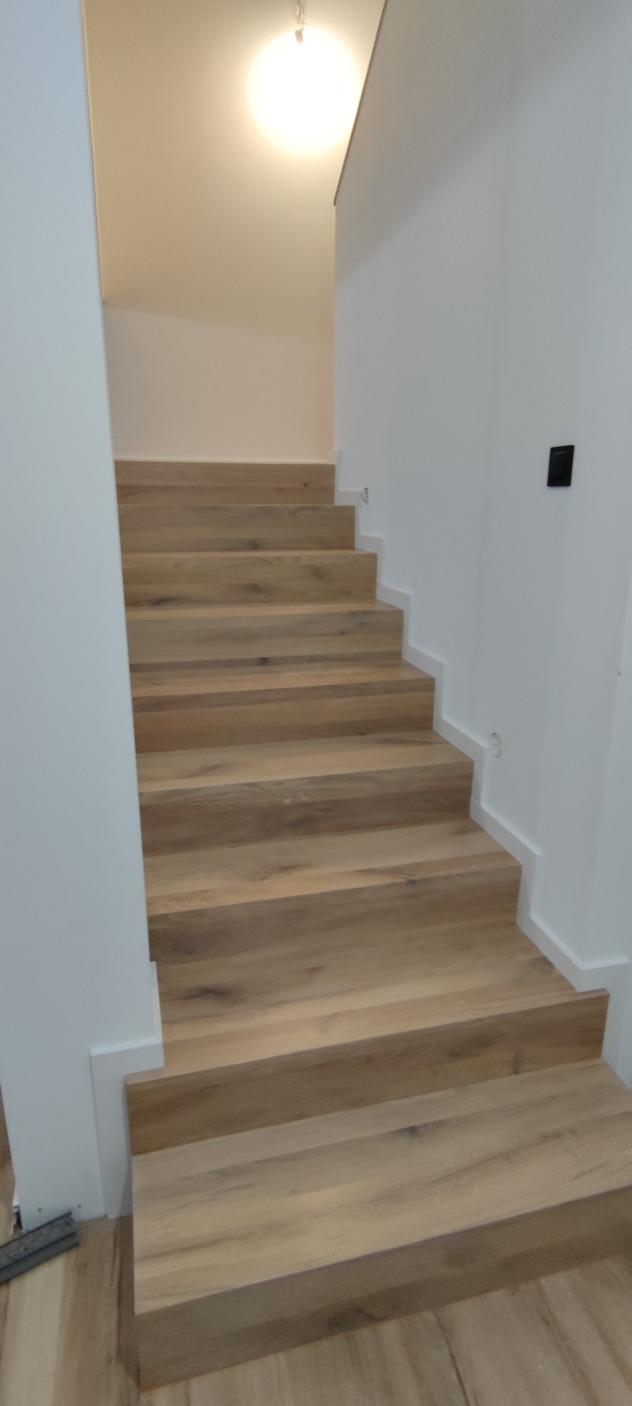 Jasne, drewniane schody w nowoczesnym wnętrzu, widok z dołu, minimalistyczne białe ściany.