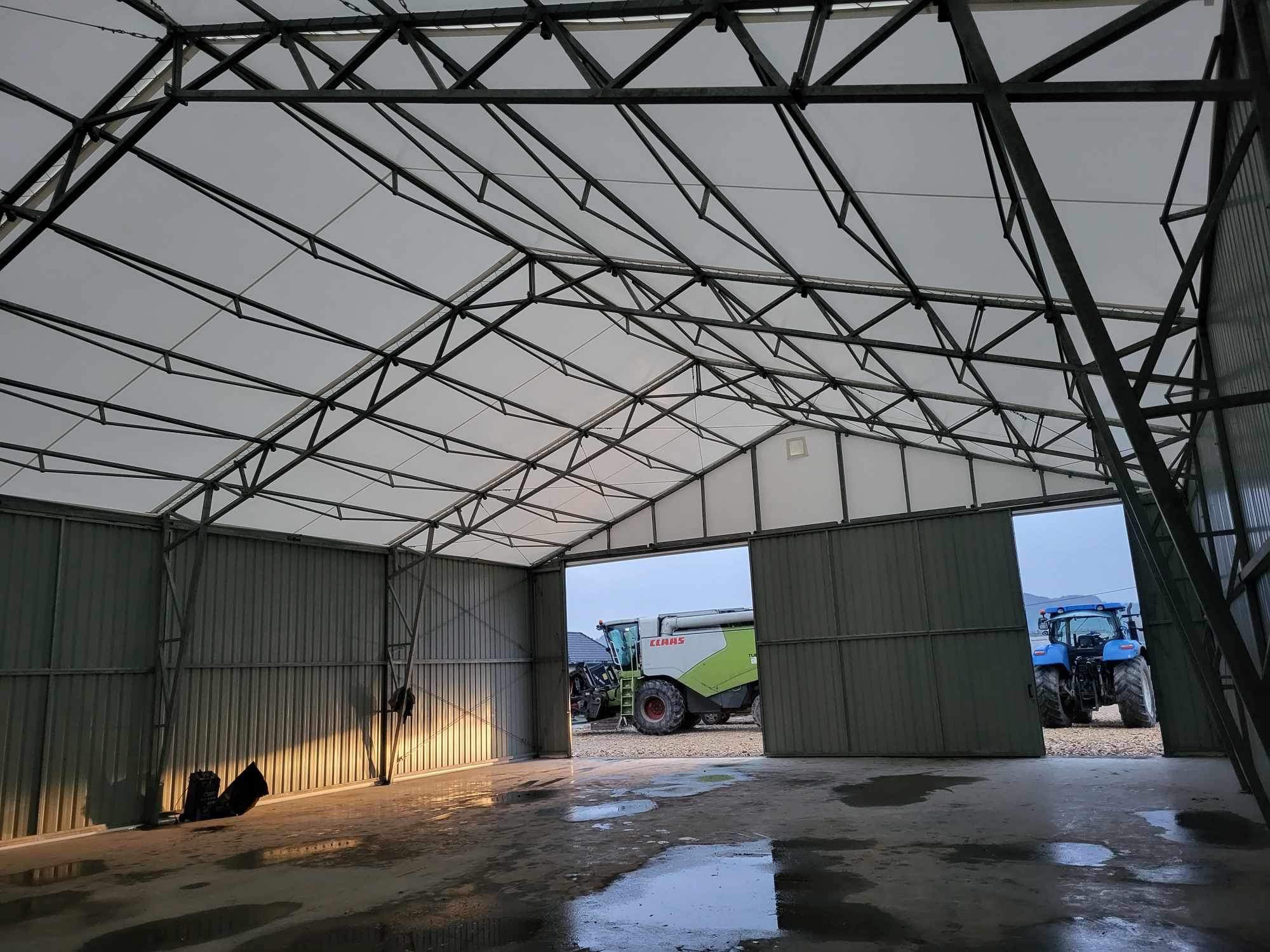 Wnętrze hali z metalową konstrukcją i białym dachem, przez otwarte wrota widoczne maszyny rolnicze: kombajn i traktor.