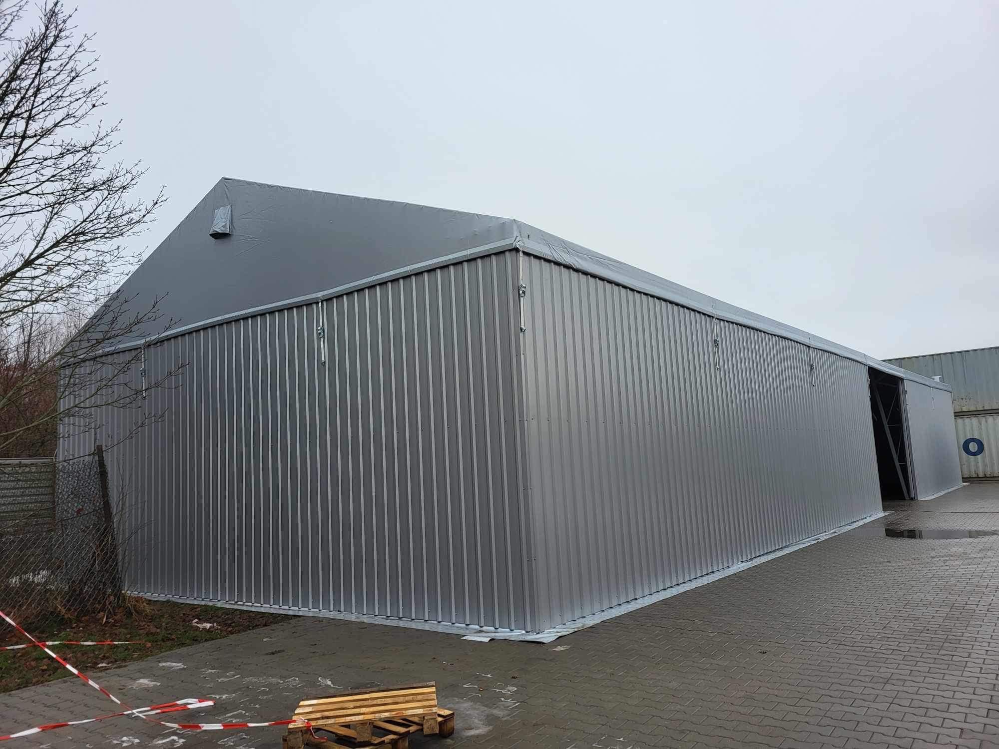 Gotowa hala magazynowa z szarej blachy trapezowej i plandekowym dachem, widoczna paleta drewniana na pierwszym planie i taśma ostrzegawcza.