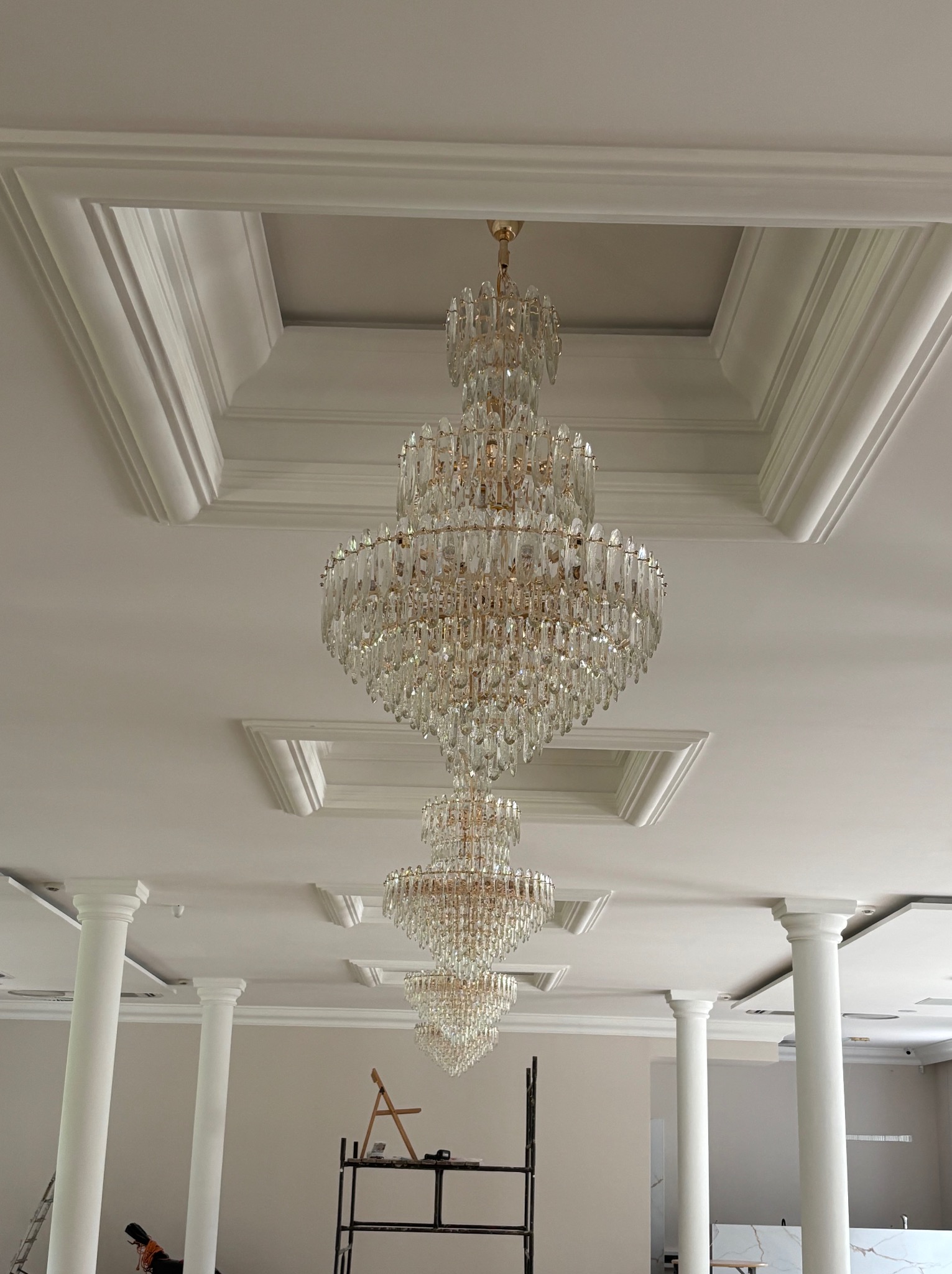 Wykończone wnętrze z kolumnami i kryształowymi żyrandolami. Widoczne sztukaterie sufitowe i drabina malarska. Całość utrzymana w jasnej kolorystyce.