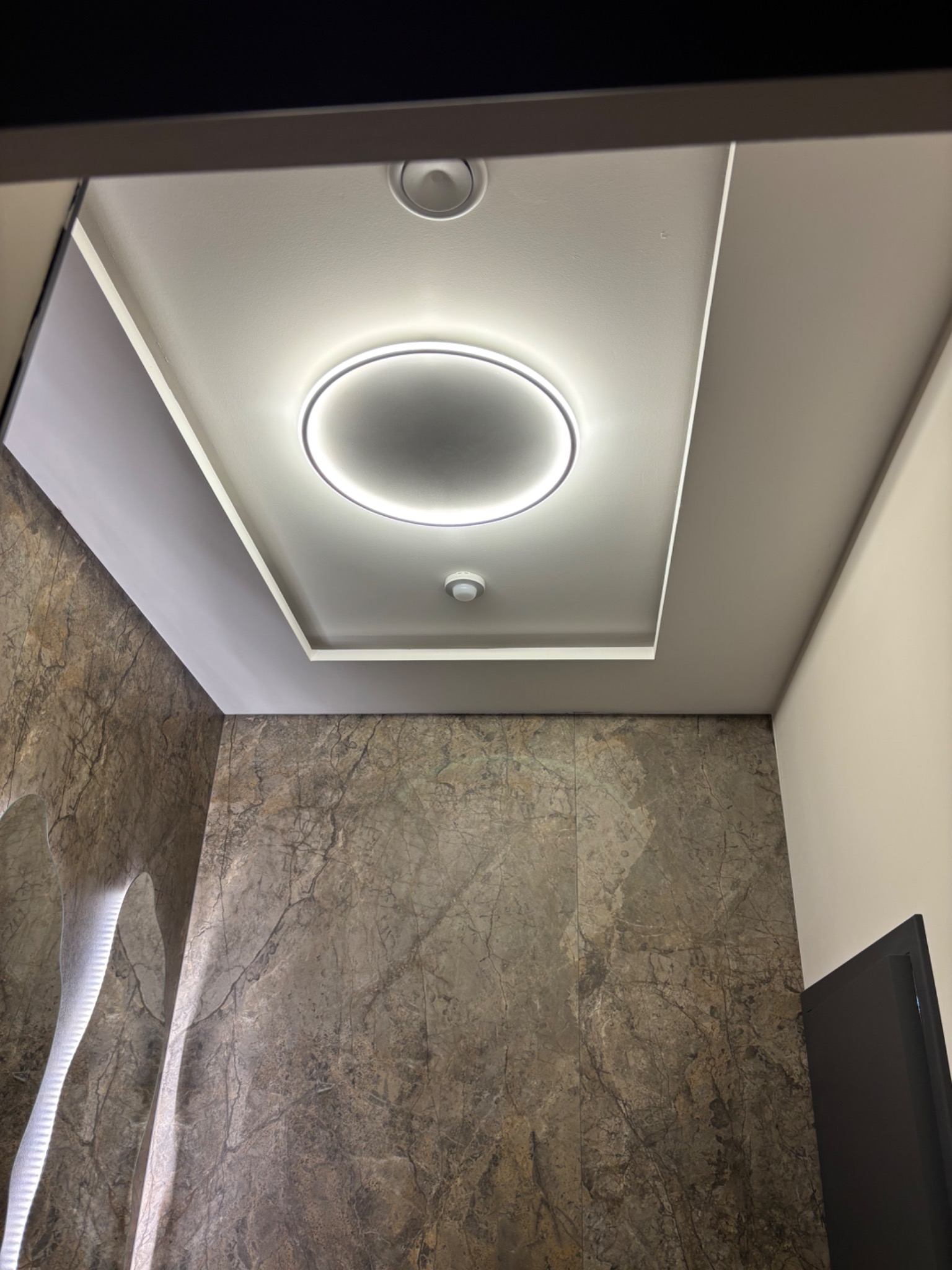 Nowoczesna łazienka z marmurową ścianą i podwieszanym sufitem z okrągłym oświetleniem LED. Minimalistyczny design i eleganckie wykończenie.