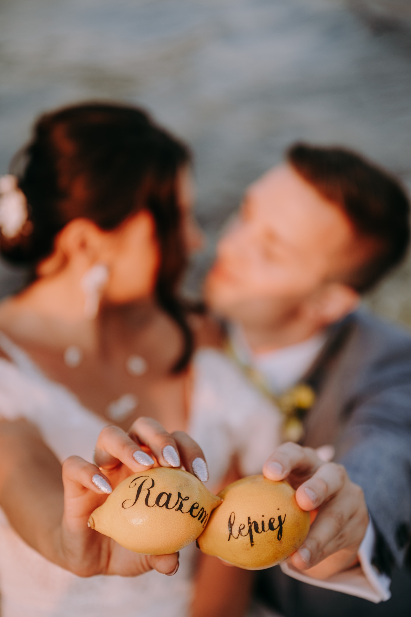 Para młoda trzyma dwa cytryny z napisem 'Razem Lepiej', tło rozmyte, ujęcie z bliska.