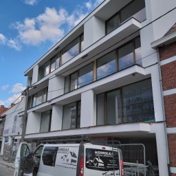 ZAKŁAD OGÓLNOBUDOWLANY Mariusz Komolka - Trzypiętrowy budynek po renowacji elewacji, widoczny z poziomu ulicy, z pracownikiem wchodzącym do firmowego busa z logo wykonawcy.