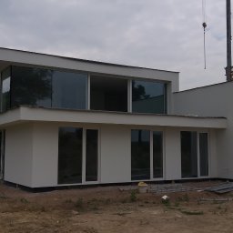 ZAKŁAD OGÓLNOBUDOWLANY Mariusz Komolka - Nowoczesny, dwukondygnacyjny dom z płaskim dachem i dużymi oknami, świeżo po wykonaniu elewacji, z widocznym żurawiem budowlanym w tle.