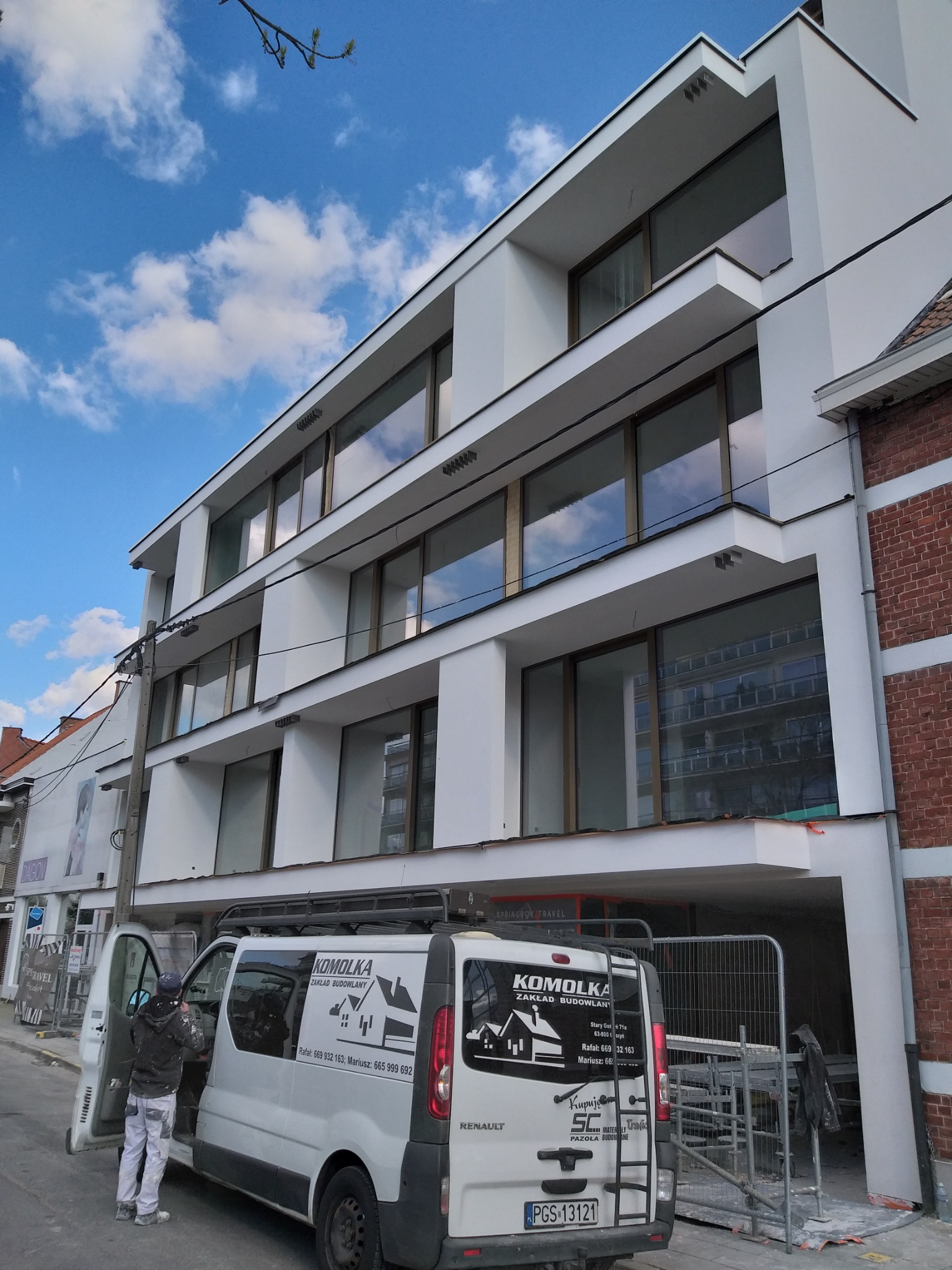 Trzypiętrowy budynek po renowacji elewacji, widoczny z poziomu ulicy, z pracownikiem wchodzącym do firmowego busa z logo wykonawcy.
