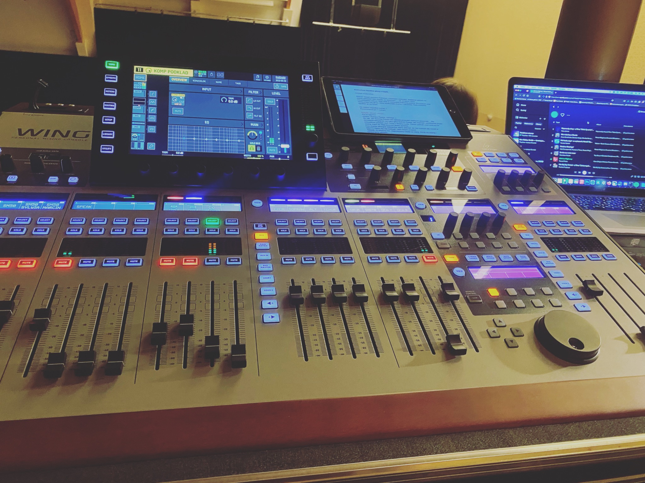 Profesjonalny mikser dźwięku WING z ekranami LCD i suwakami, ustawiony w pomieszczeniu z laptopem i tabletem, gotowy do miksowania muzyki.