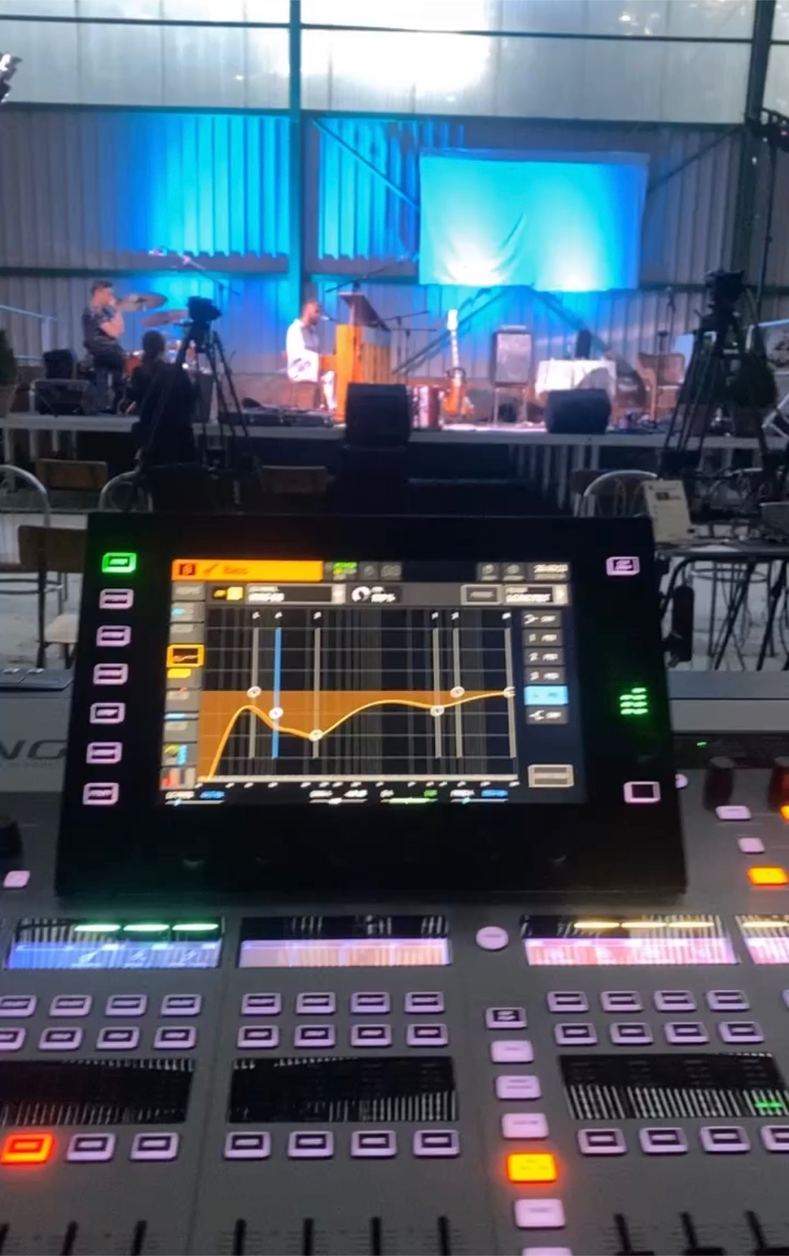 Konsoleta dźwiękowa z widocznym ekranem equalizera podczas koncertu na scenie z muzykami w tle.