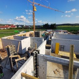 GOSYMAR SPÓŁKA Z OGRANICZONĄ ODPOWIEDZIALNOŚCIĄ - Budowa domu z bloczków betonu komórkowego, widok z góry na fundamenty i ściany parteru, z żurawiem budowlanym w tle i pracownikiem w kasku.
