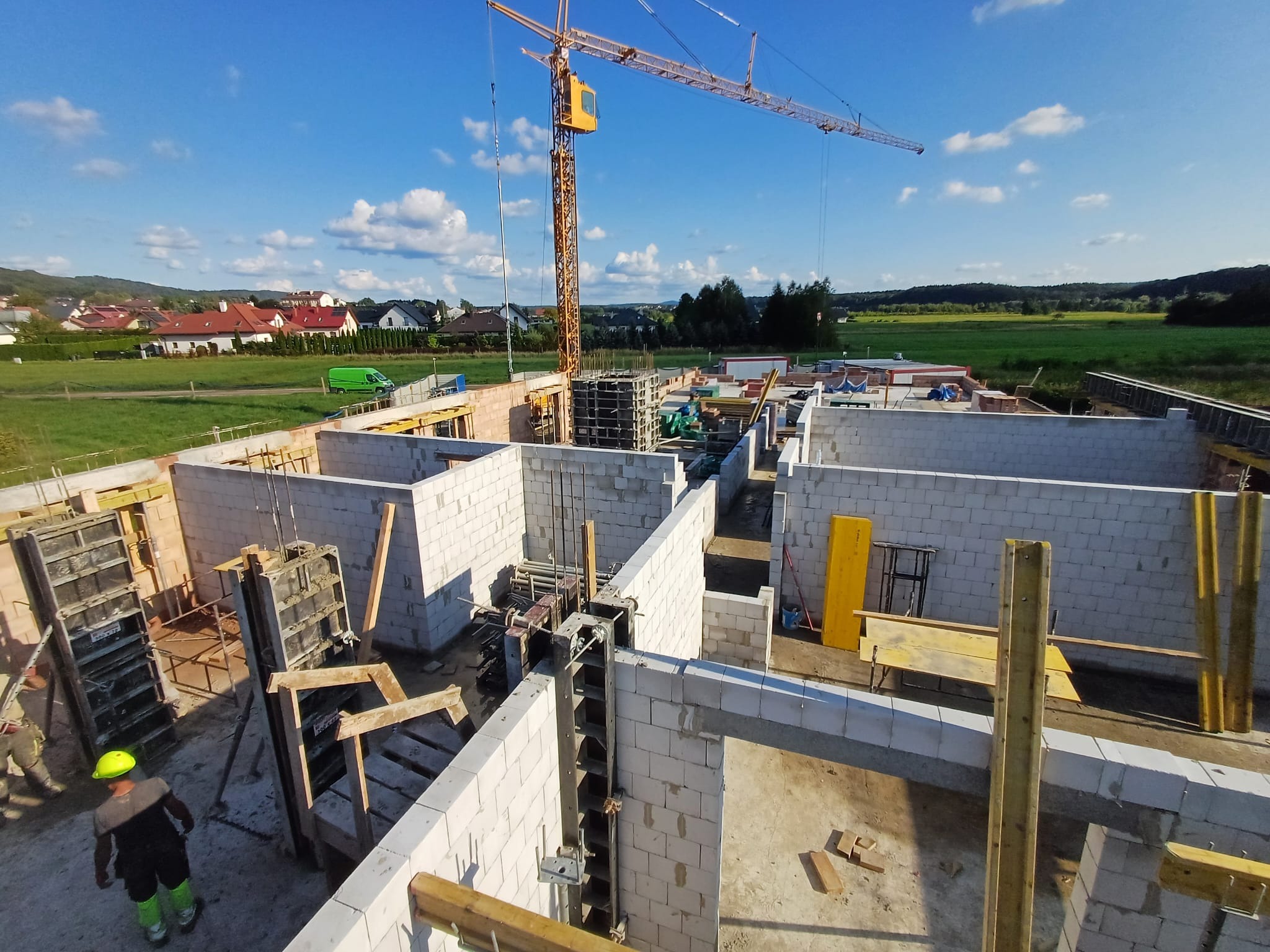 Budowa domu z bloczków betonu komórkowego, widok z góry na fundamenty i ściany parteru, z żurawiem budowlanym w tle i pracownikiem w kasku.