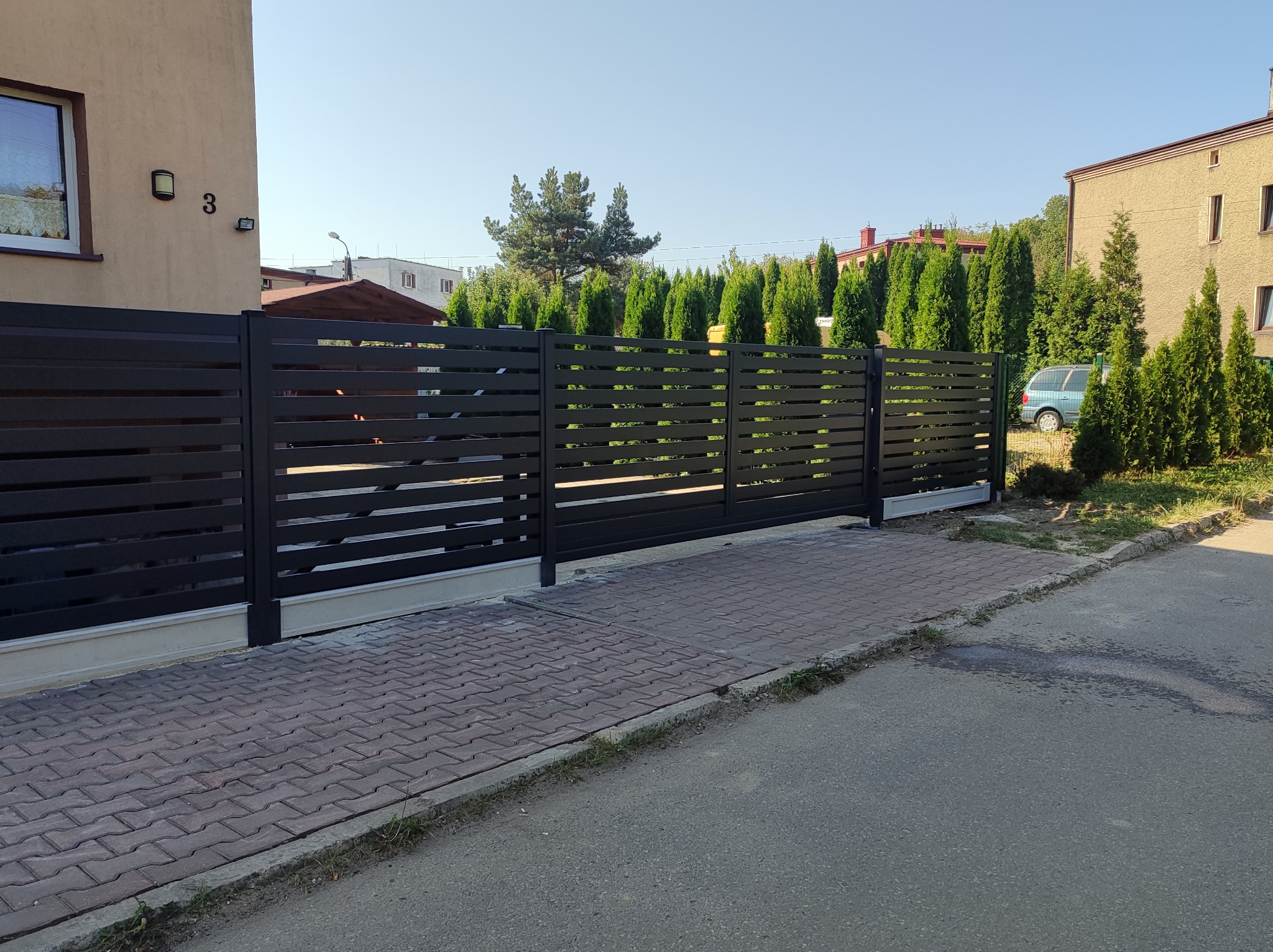 Nowoczesna, pozioma, przesuwna brama wjazdowa w kolorze antracytowym, z widocznym numerem domu '3' i kostką brukową na podjeździe.