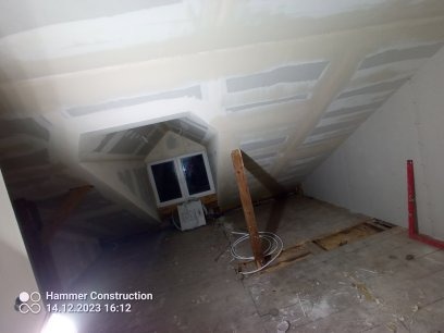 Poddasze w trakcie prac wykończeniowych: zamontowane płyty gipsowo-kartonowe na skosach sufitu, okno dachowe w zabudowie, widoczne elementy konstrukcji drewnianej i poziomica.