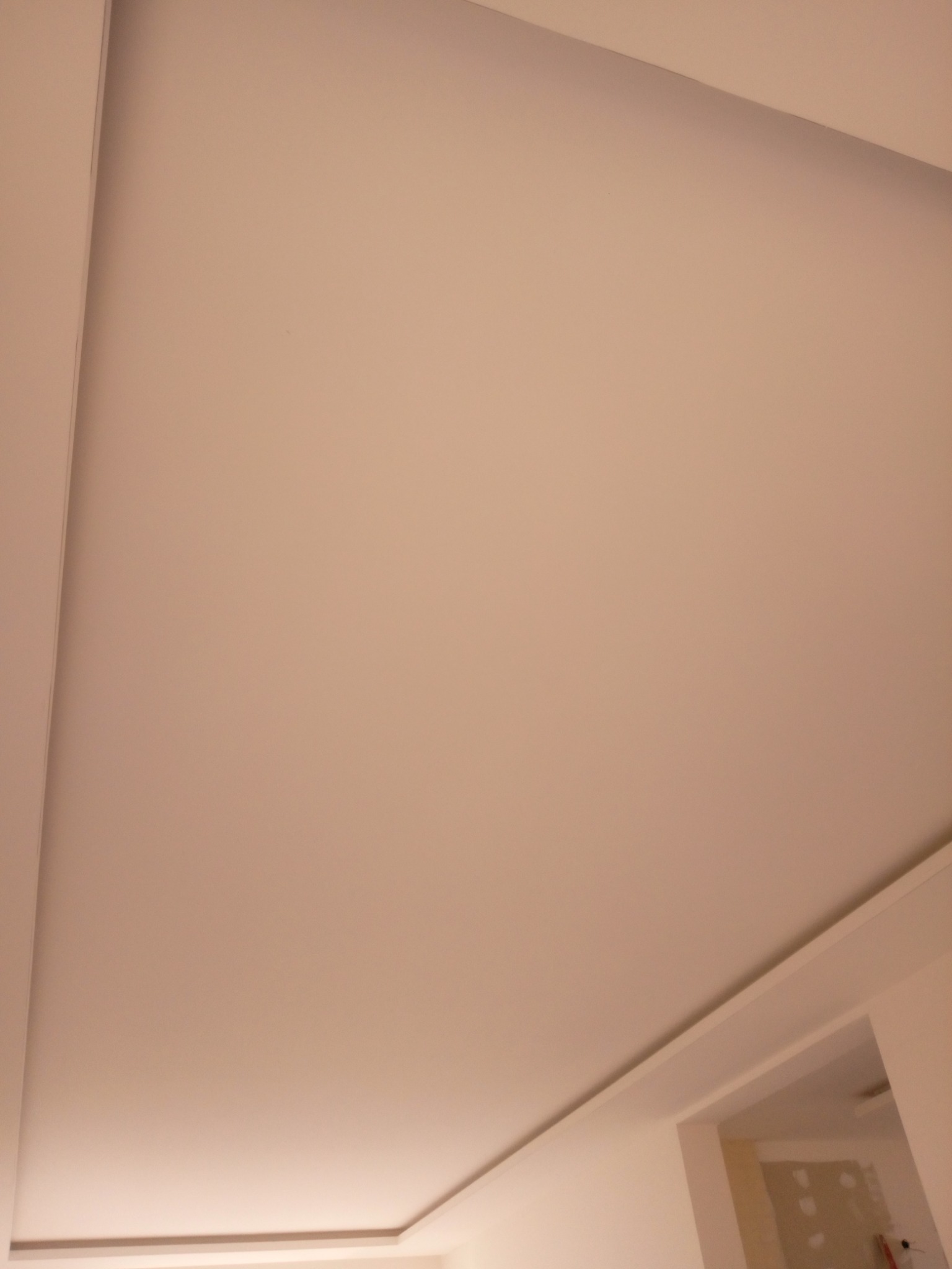 Gładka, beżowa powierzchnia sufitu podwieszanego z delikatnym oświetleniem LED wzdłuż krawędzi, widok z dołu.