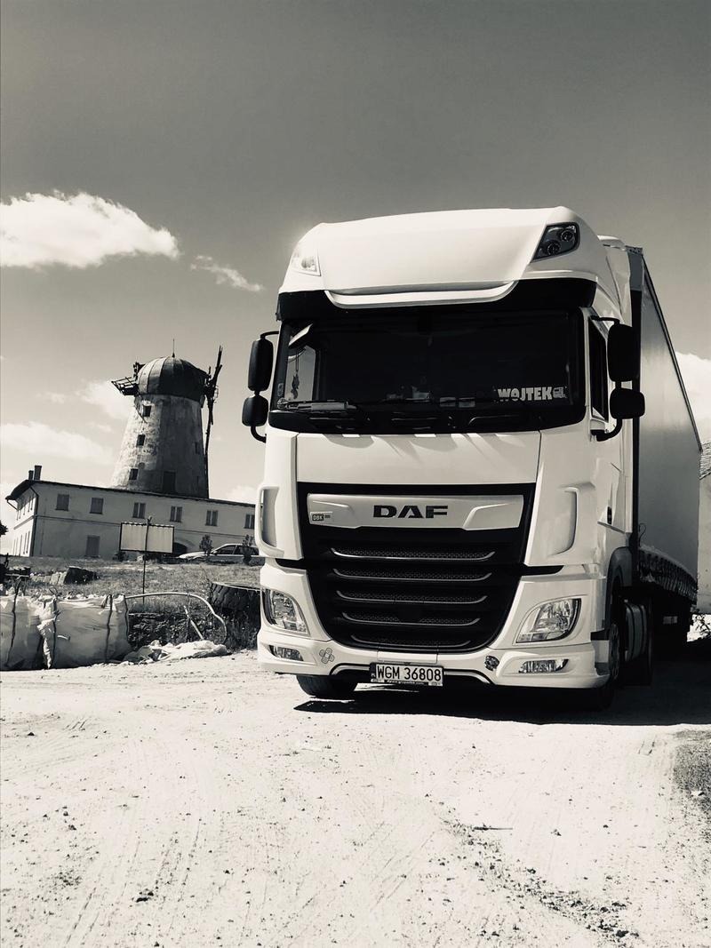Czarno-białe zdjęcie białej ciężarówki DAF z widoczną tablicą rejestracyjną WGM 36808 na tle starego młyna i budynku, przy pochmurnym niebie.