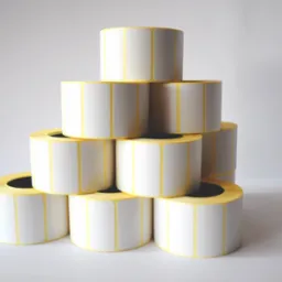 Piramida z rolek białych naklejek z żółtymi krawędziami, na jasnym tle.