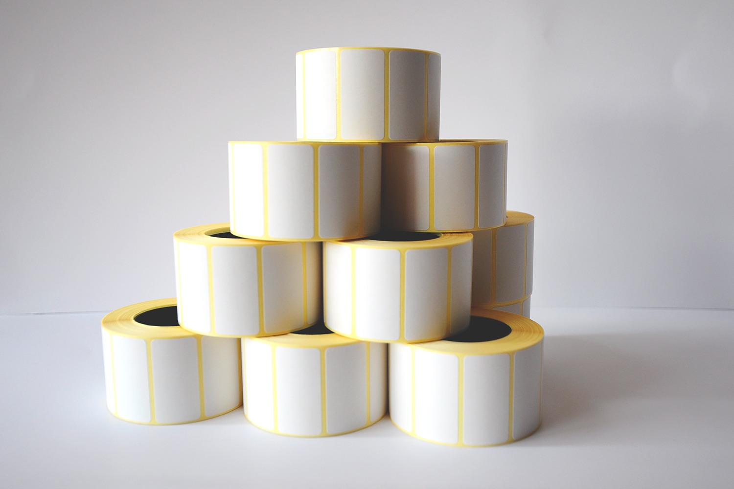 Piramida z rolek białych naklejek z żółtymi krawędziami, na jasnym tle.