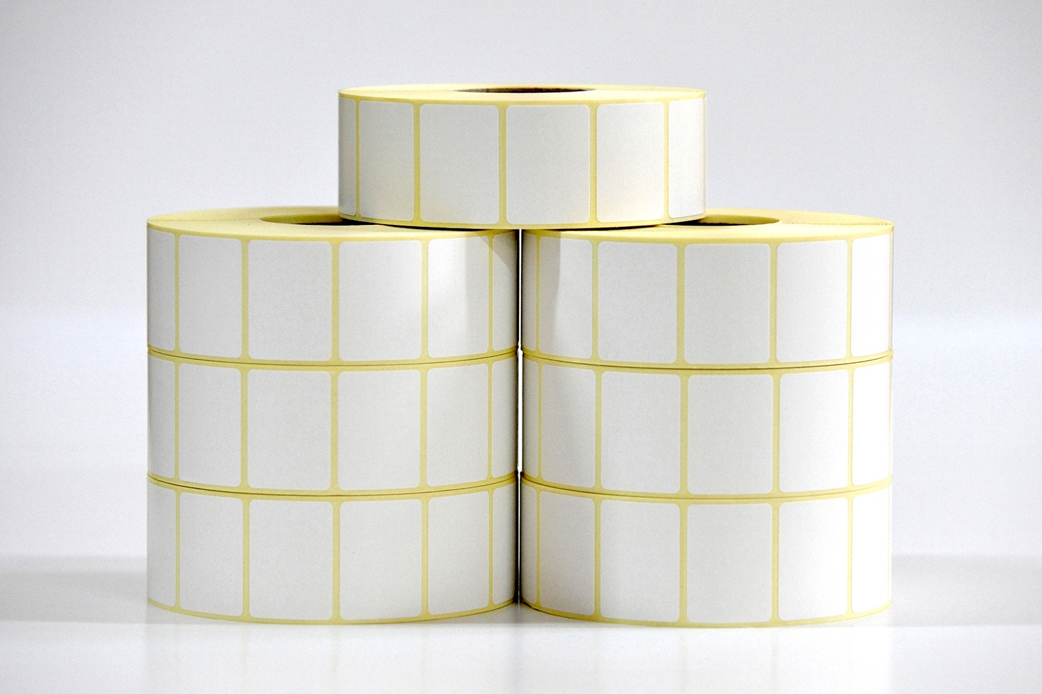 Stos rolek z białymi, prostokątnymi etykietami z żółtymi obramowaniami, ułożonych w piramidę na jasnym tle.