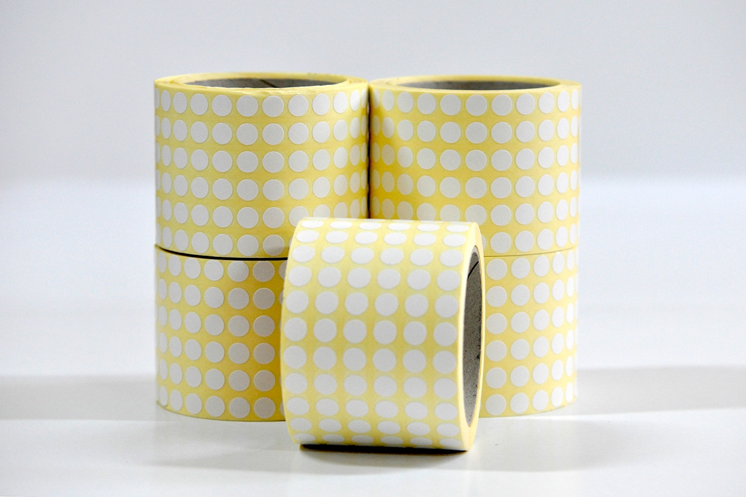 Stos rolek z żółtymi okrągłymi naklejkami na białym tle, jedna rolka leży poziomo na pierwszym planie.