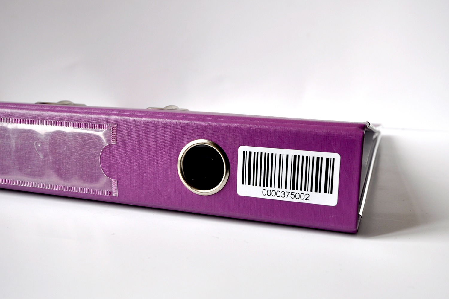 Fioletowy segregator z naklejoną etykietą z kodem kreskowym 0000375002, widoczne metalowe okucie i przezroczysta kieszeń na etykietę.