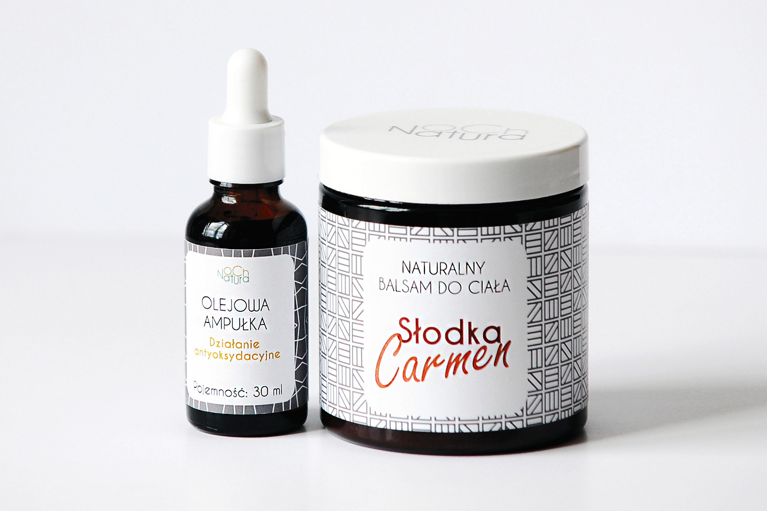 Dwa produkty kosmetyczne na białym tle: ciemna szklana buteleczka z pipetą i etykietą 'Olejowa Ampułka' oraz okrągły słoik z białym wieczkiem i etykietą 'Naturalny Balsam do Ciała Słodka Carmen'.