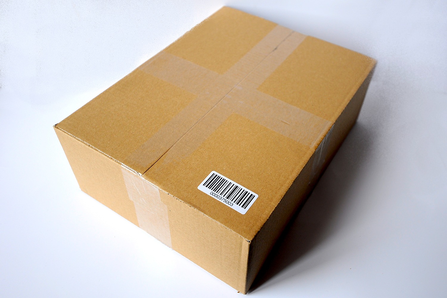 Zamknięte kartonowe pudełko z naklejoną etykietą z kodem kreskowym, zabezpieczone przezroczystą taśmą na białym tle.