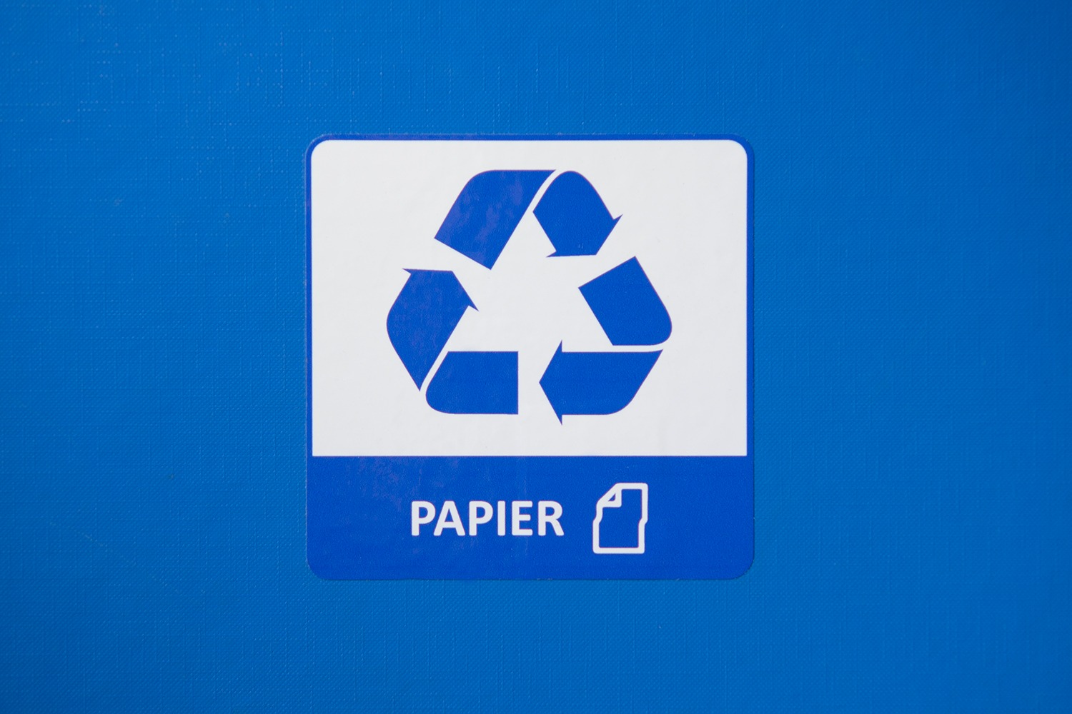 Niebieska naklejka na pojemniku z symbolem recyklingu papieru i napisem 'PAPIER' oraz ikoną kartki.