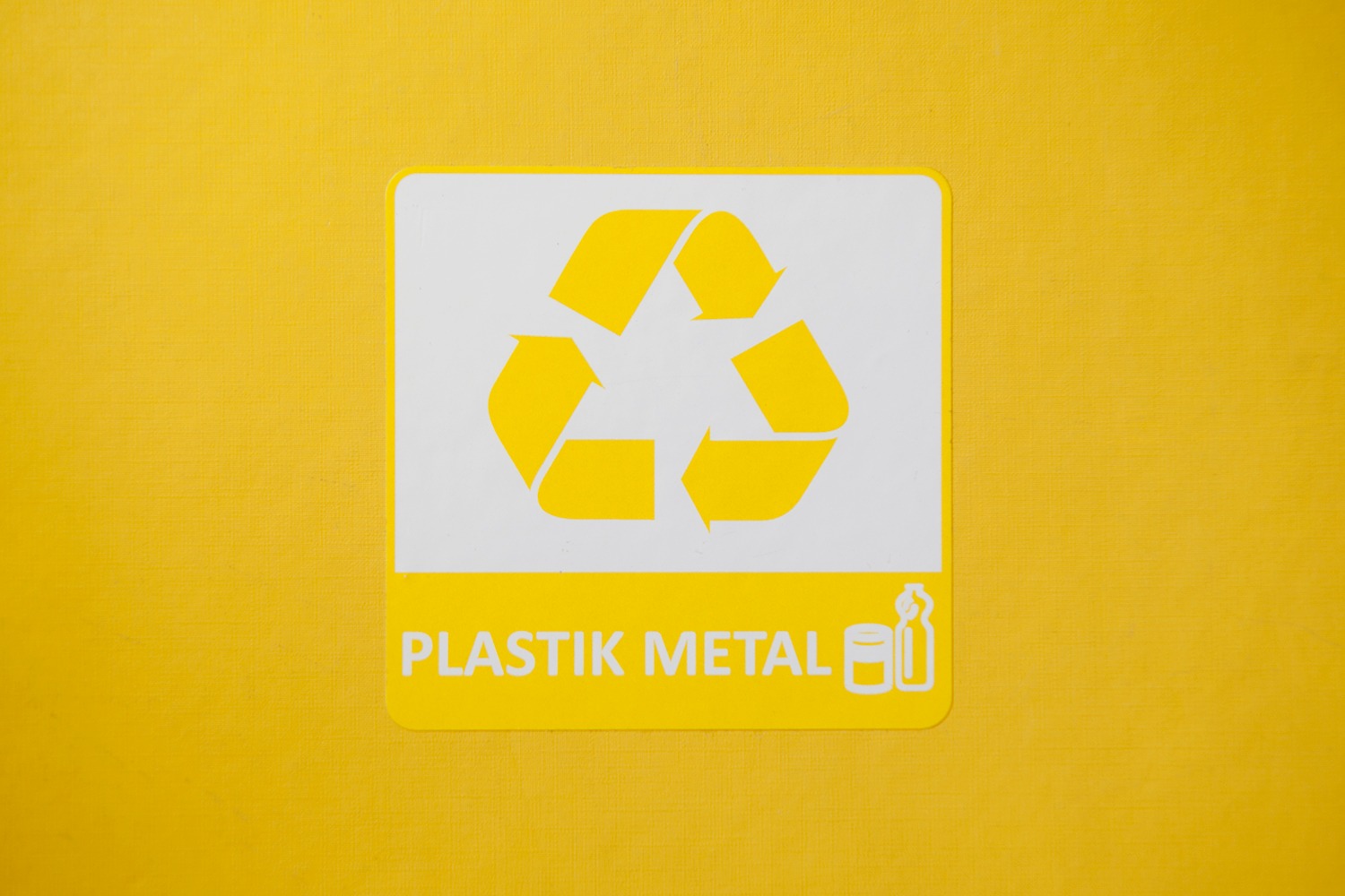 Żółta naklejka z symbolem recyklingu i napisem 'PLASTIK METAL' umieszczona na żółtym tle.