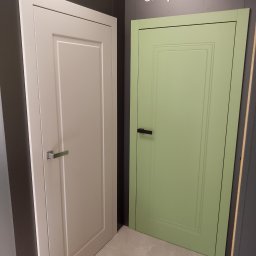 PRZESTRZEŃ KREACJI SPÓŁKA Z OGRANICZONĄ ODPOWIEDZIALNOŚCIĄ - Wystawa dwóch modeli drzwi wewnętrznych: kremowe z kwadratowym panelem i srebrną klamką oraz pistacjowe z prostokątnym panelem i czarną klamką, obok napis Simple Door.