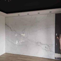 33M2 Sp. z o.o. - Wykończona ściana w pomieszczeniu z płytami imitującymi marmur, widoczny grzejnik elektryczny i drewnopodobna podłoga.