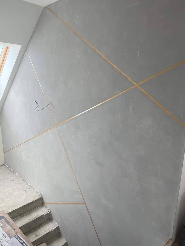 Ściana z szarą gładzią i złotymi liniami dekoracyjnymi w Stargardzie, widoczne schody i okno dachowe.