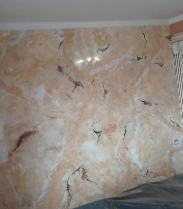 Ściana z dekoracyjną, marmurkową fakturą w odcieniach beżu i bieli, z ciemnymi żyłkami, zabezpieczona folią malarską u dołu.