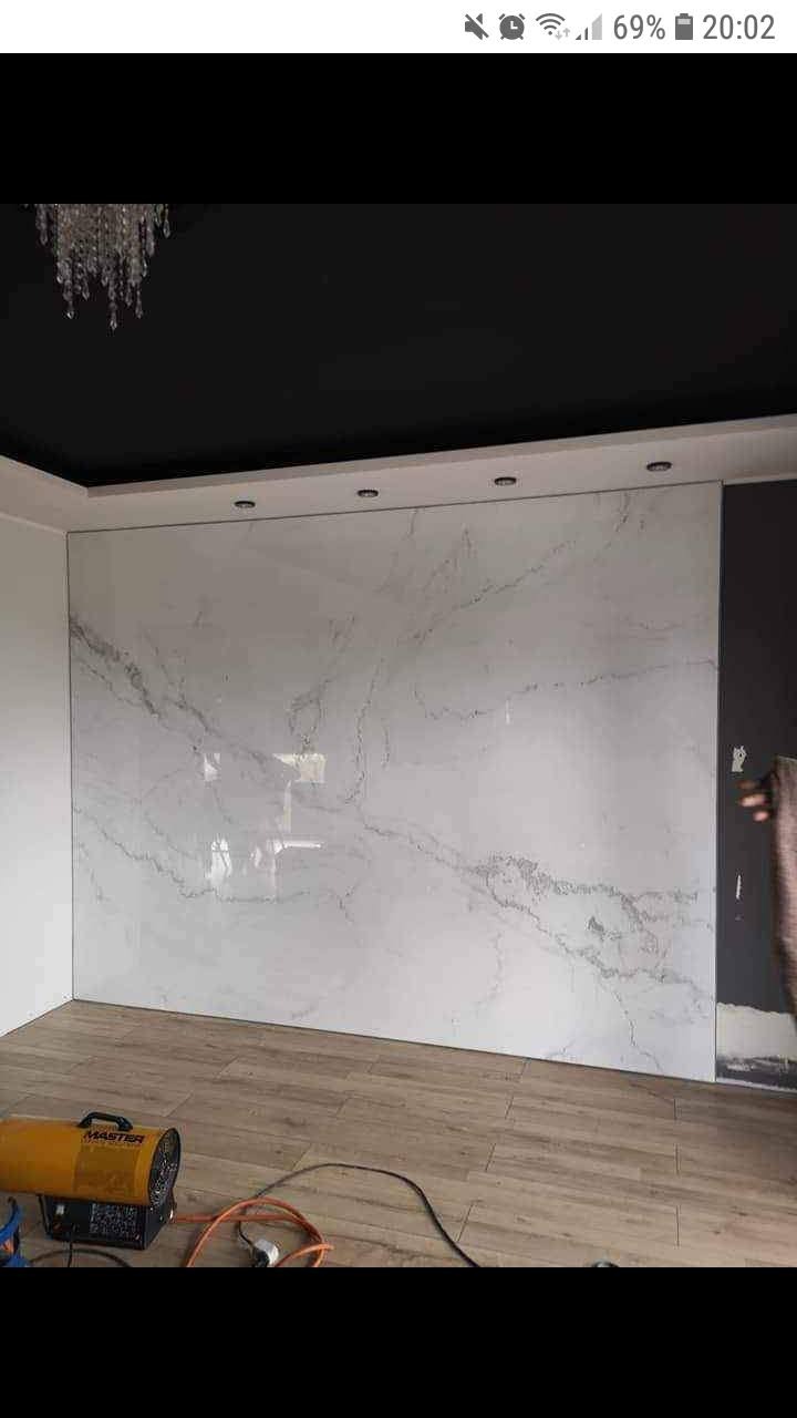 Wykończona ściana w pomieszczeniu z płytami imitującymi marmur, widoczny grzejnik elektryczny i drewnopodobna podłoga.