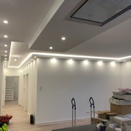 Foreman - Nowoczesne wykończenie wnętrza: białe ściany, sufit z oświetleniem LED, widoczne kartony i narzędzia, jasna podłoga. Minimalistyczny design w trakcie prac.