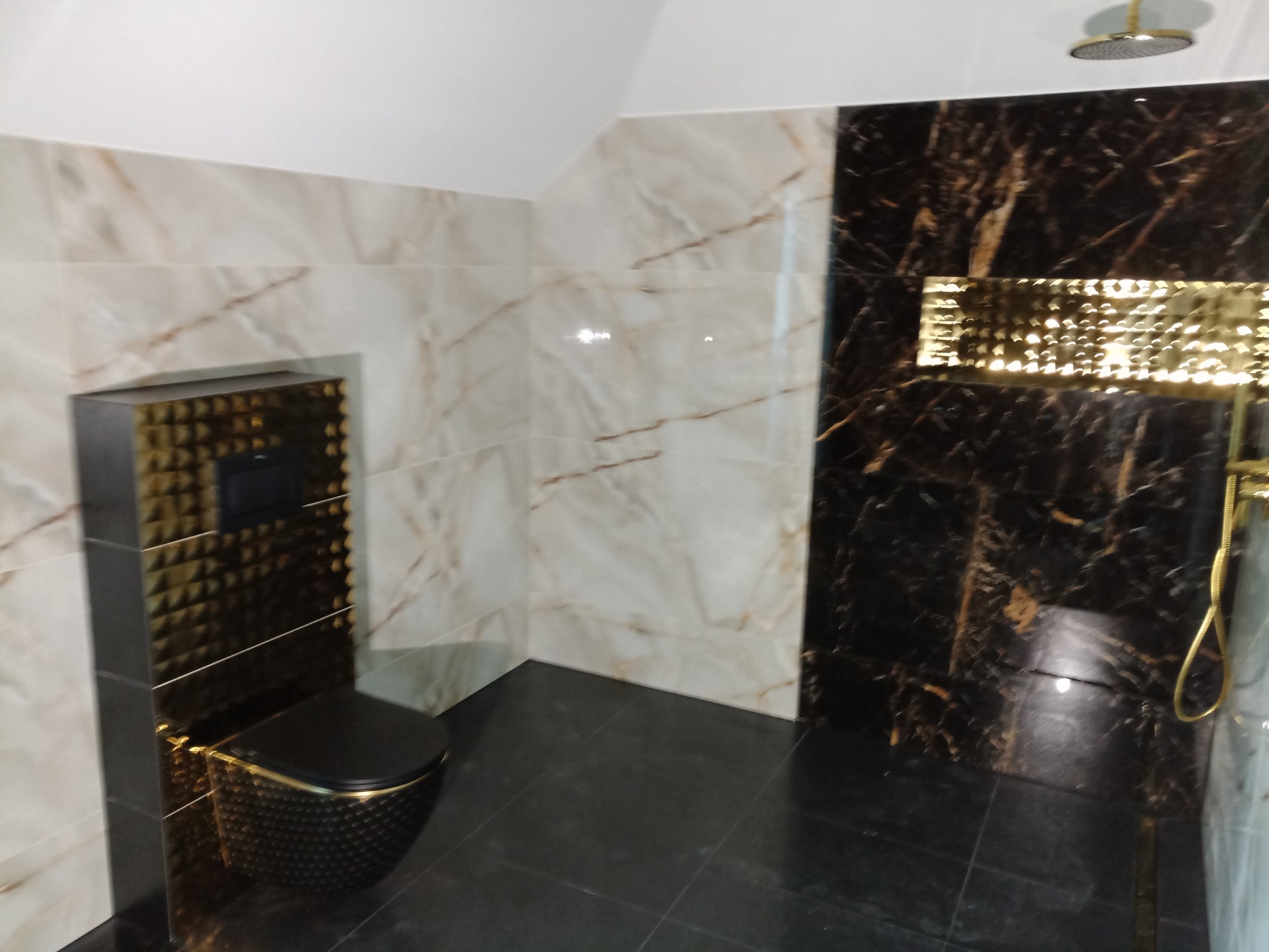 Luksusowa łazienka z czarną armaturą i złotymi akcentami, marmurowe płytki na ścianach i podłodze, deszczownica zamontowana na suficie.