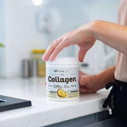 Fotografia i wideografia reklamowa Szymon Kryszczak - Kobieta otwiera opakowanie kolagenu Olimp Labs na blacie kuchennym z elementami zlewu w tle.