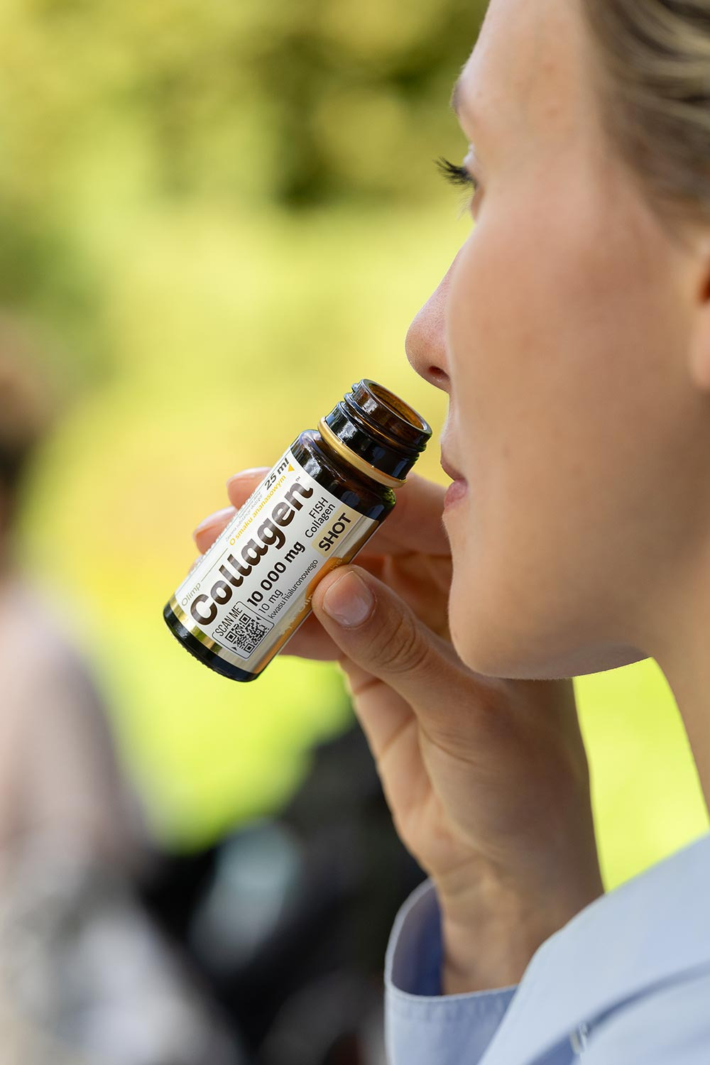 Kobieta pije shot kolagenowy z małej butelki, widoczny profil twarzy i etykieta produktu z QR kodem.